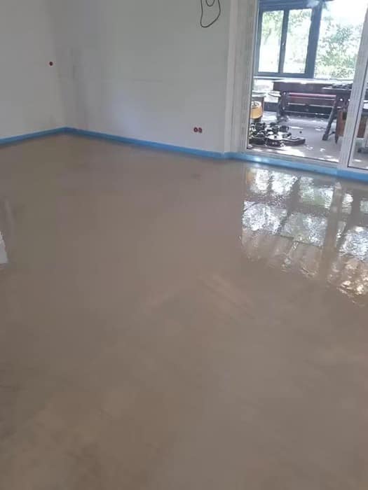 Șapa autonivelantă întinsă și încă lucioasă, cu banda perimetrală albastră vizibilă pe tot conturul camerei