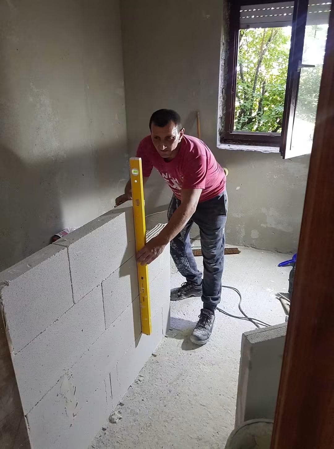 Zidar verificând cu nivela un perete nou din BCA, într-o cameră aflată în renovare